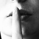 Black and white image of a finger against a woman’s lips