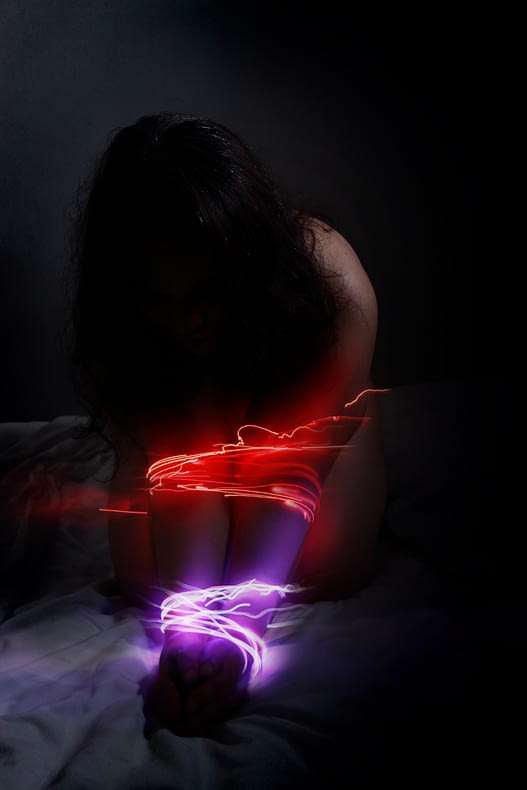 A low-light photo - I'm kneeling, bent forward with my arms in front. It looks like there are ropes of light binding my arms together, purple around my wrists and red below my elbows