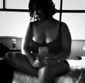 Black and white photo of me seen in mirror sitting on bed in my underwear looking at phone